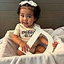 Arabella is registered to the contest to win money with this photo: toddler, child, girl, curly_hair, white_bows, blanket, letter_d, shirt, daddys_girl, sitting, indoor, portrait, cute, smiling, baby, soft_texture, cozy, person, furniture, wall