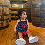 Arabella joined the competition — help win amazing prizes! toddler, child, smiling, curly_hair, dress, sneakers, wooden_floor, barrels, indoor, playful, happy, sitting, headband, earrings, casual_clothing, cute, portrait, person, bright, rustic