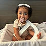 baby, pacifier, blanket, basket, curly_hair, bow, letter, wooden_headboard, indoor, cute, child, smiling, seated, soft_texture, infant, holding, light_skin, portrait, cozy, home