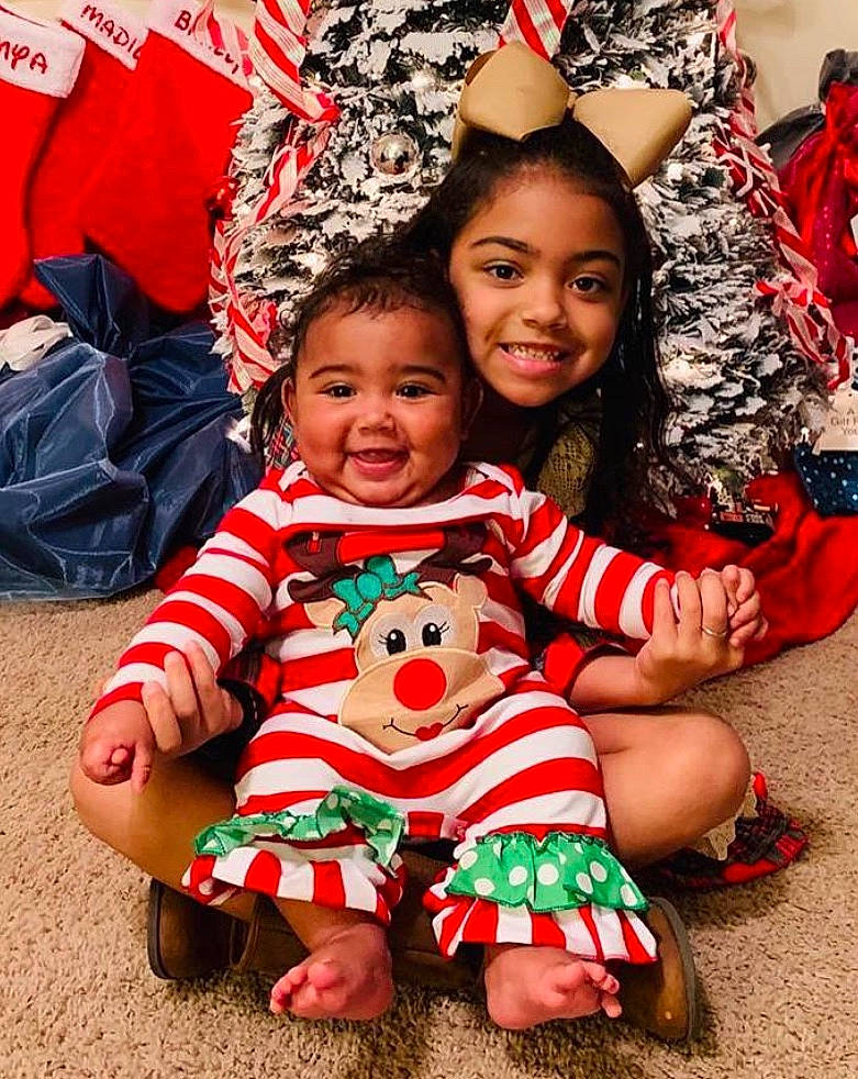 Braelyn is registered to the contest to win money with this photo: baby, child, christmas, christmas_decoration, christmas_eve, christmas_tree, event, family, fictional_character, fun, happy, head, holiday, joy, people, person, play, red, sitting, smile
