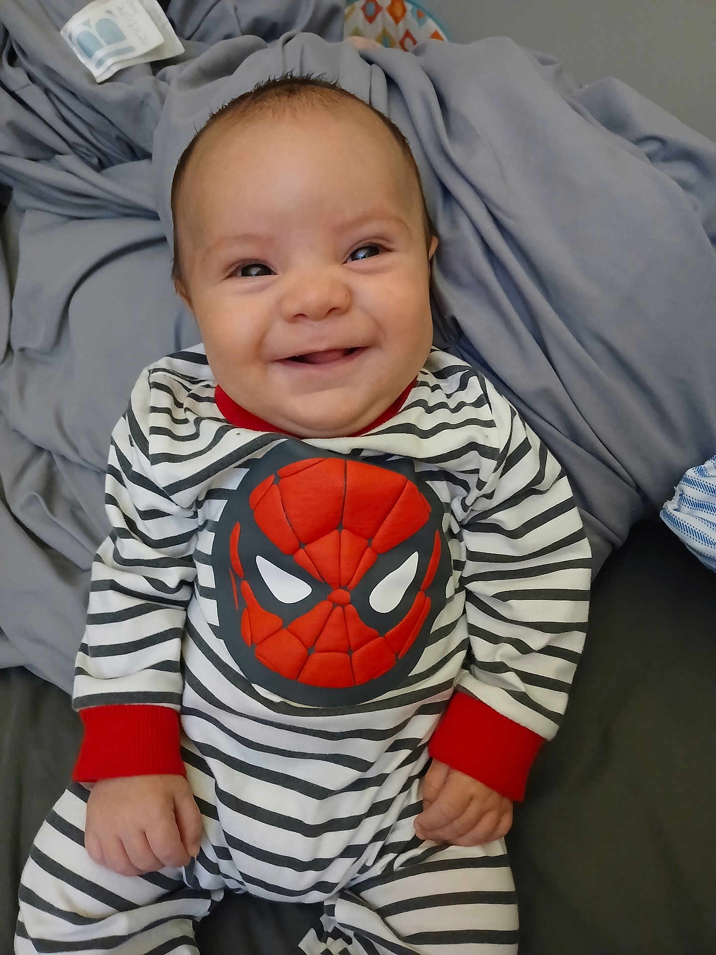 Oliver joined the competition — help win amazing prizes! baby, smiling, striped_clothing, onesie, spiderman, infant, child, cute, happy, indoors, blanket, soft, wrinkled, comfort, portrait, person, chubby_cheeks, casual, seated, young