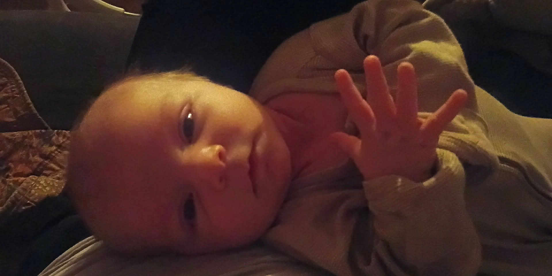 Timothy is registered to the contest to win money with this photo: baby, infant, face, hand, fingers, clothing, portrait, closeup, lying_down, expression, skin, person, young_child, indoor, warm_lighting, cozy, newborn, baby_garment, head, resting