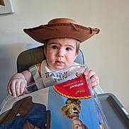 Caysen joined the competition — help win amazing prizes! baby, child, cowboy_hat, high_chair, portrait, sitting, indoors, face, eyes, tongue, smiling, toy_story, woody, toy, tray, bib, feeding, brown_hat, playful, photography