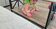 Caysen is registered to the contest to win money with this photo: baby, books, child, coffee_table, diaper, fireplace, floor, furniture, green_outfit, home, indoor, infant, living_room, portrait, shelf, sitting, smiling, sofa, toy, wood