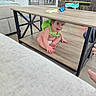 baby, child, infant, smiling, sitting, indoor, living_room, coffee_table, shelf, furniture, sofa, books, toy, home, floor, wood, fireplace, green_outfit, diaper, portrait