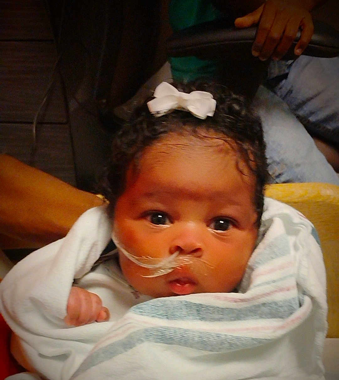Nova joined the competition — help win amazing prizes! baby, infant, blanket, bow, curly_hair, nasal_tube, wrapped, wide_eyes, person, child, cute, newborn, indoor, holding, face, skin, expression, young, healthcare, comfort