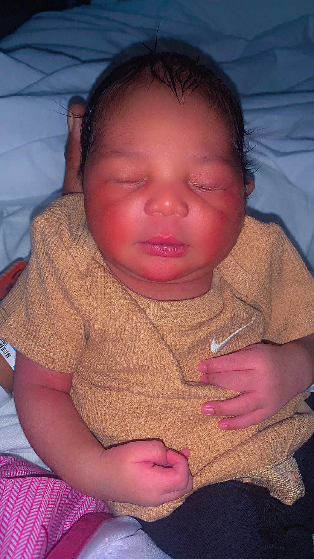 Adrian joined the competition — help win amazing prizes! baby, newborn, sleeping, infant, clothing, beige_shirt, nike_logo, hand, fist, bed, blanket, person, face, skin, cute, resting, indoors, soft_lighting, portrait, child