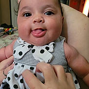 Karmen is registered to the contest to win money with this photo: baby, child, face, tongue, polka_dot, dress, hand, indoor, person, cute, playful, smile, closeup, cheeks, infant, striped, holding, skin, human, apparel