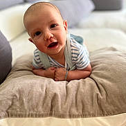 Lucas joined the competition — help win amazing prizes! baby, infant, pillow, cushion, face, smile, child, indoor, soft, cozy, striped_clothing, person, head, eyes, happy, young_child, living_room, blurred_background, skin, arm
