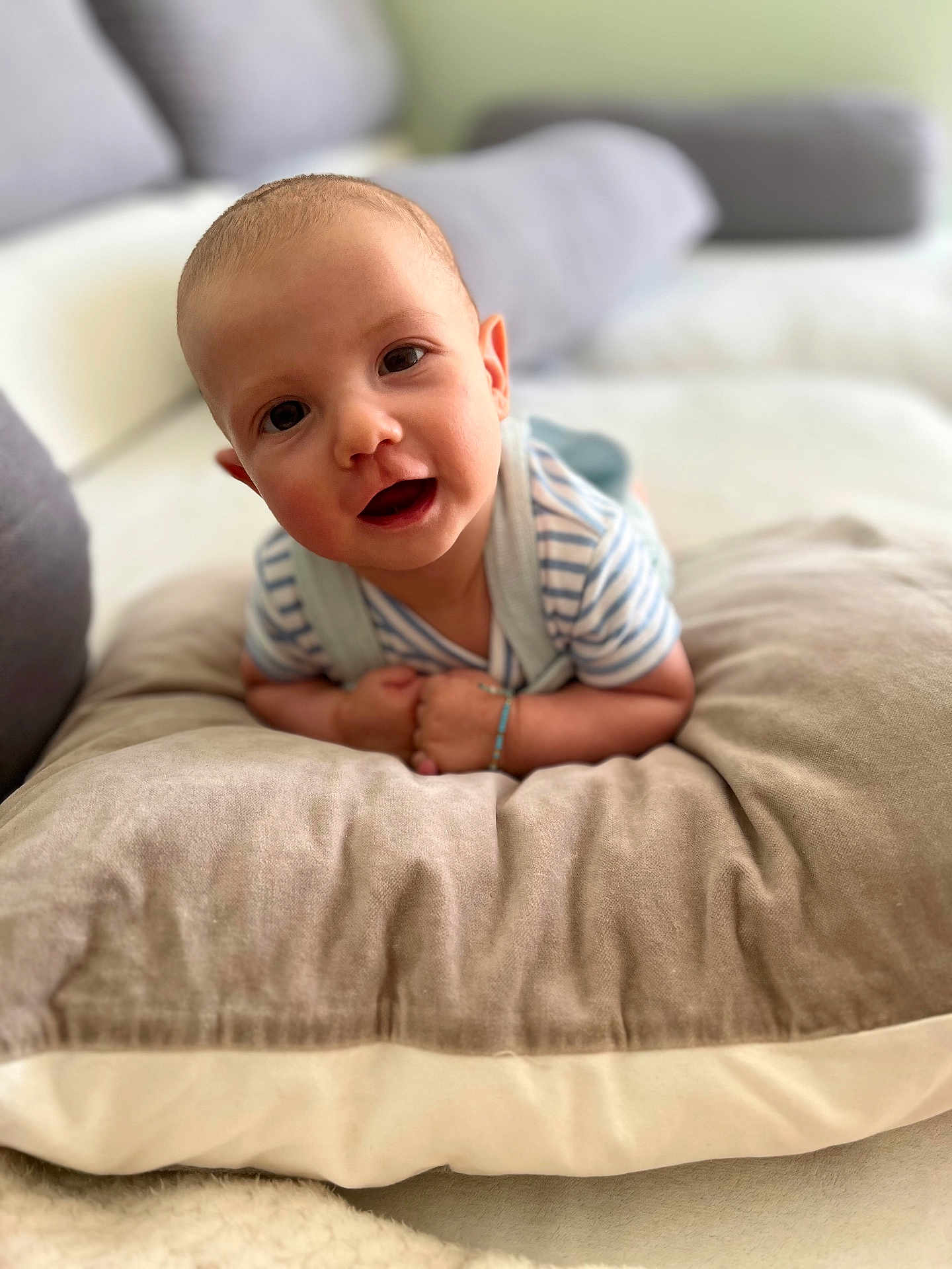 Lucas joined the competition — help win amazing prizes! baby, infant, pillow, cushion, face, smile, child, indoor, soft, cozy, striped_clothing, person, head, eyes, happy, young_child, living_room, blurred_background, skin, arm