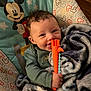baby, child, smiling, blanket, toy, teething_toy, mickey_mouse, seat, curly_hair, happy, indoor, infant, clothing, person, cute, playful, comfort, colorful, young_child, portrait