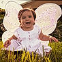 Isabella is registered to the contest to win money with this photo: toddler, child, grass, fairy_wings, costume, smiling, happy, outdoor, sunlight, dress, playful, cute, nature, portrait, baby, young_child, sitting, greenery, daylight, fun