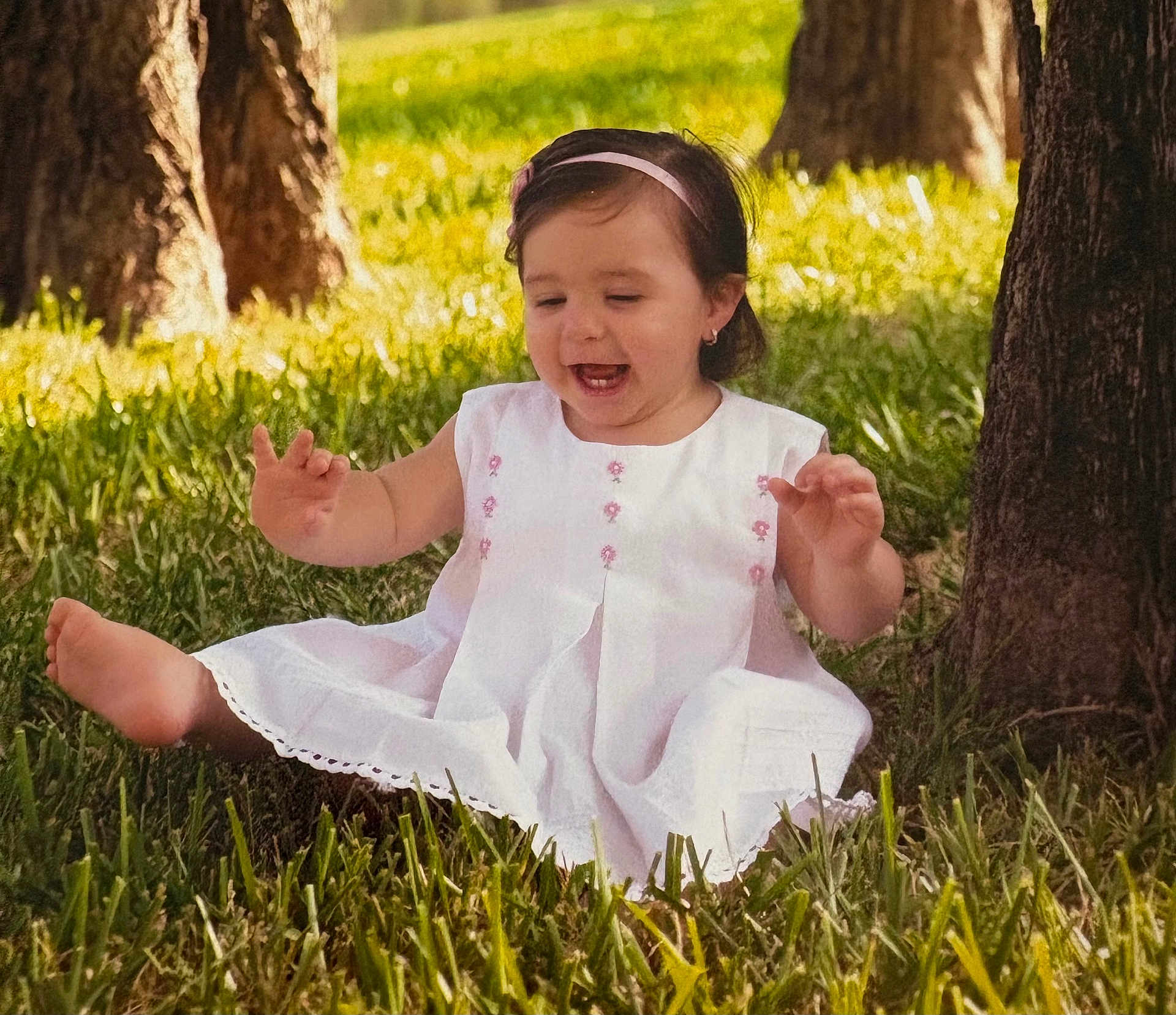 Isabella joined the competition — help win amazing prizes! toddler, child, grass, tree, outdoor, nature, smiling, happy, white_dress, barefoot, headband, sunlight, greenery, playful, sitting, young_child, portrait, daylight, cute, joyful