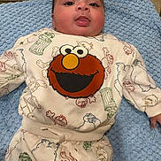 Makari is registered to the contest to win money with this photo: baby, infant, child, face, tongue, blue_blanket, clothing, elmo, sesame_street, cute, lying_down, indoors, sleepsuit, patterned_clothing, playful, portrait, young_child, soft_texture, smiling, cozy