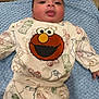 baby, infant, child, face, tongue, blue_blanket, clothing, elmo, sesame_street, cute, lying_down, indoors, sleepsuit, patterned_clothing, playful, portrait, young_child, soft_texture, smiling, cozy