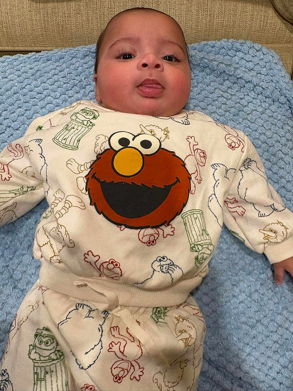 Makari is registered to the contest to win money with this photo: baby, infant, child, face, tongue, blue_blanket, clothing, elmo, sesame_street, cute, lying_down, indoors, sleepsuit, patterned_clothing, playful, portrait, young_child, soft_texture, smiling, cozy