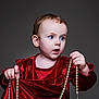 child, toddler, baby, blue_eyes, red_dress, velvet, pearl_necklace, portrait, studio_lighting, curly_hair, expression, holding, jewelry, fashion, cute, indoor, person, closeup, face, curiosity