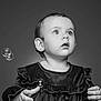 Josie is registered to the contest to win money with this photo: child, toddler, portrait, black_and_white, bubbles, curious, expression, clothing, long_sleeves, ruffles, hands, studio, soft_lighting, face, eyes, hair, innocence, looking_up, monochrome, baby