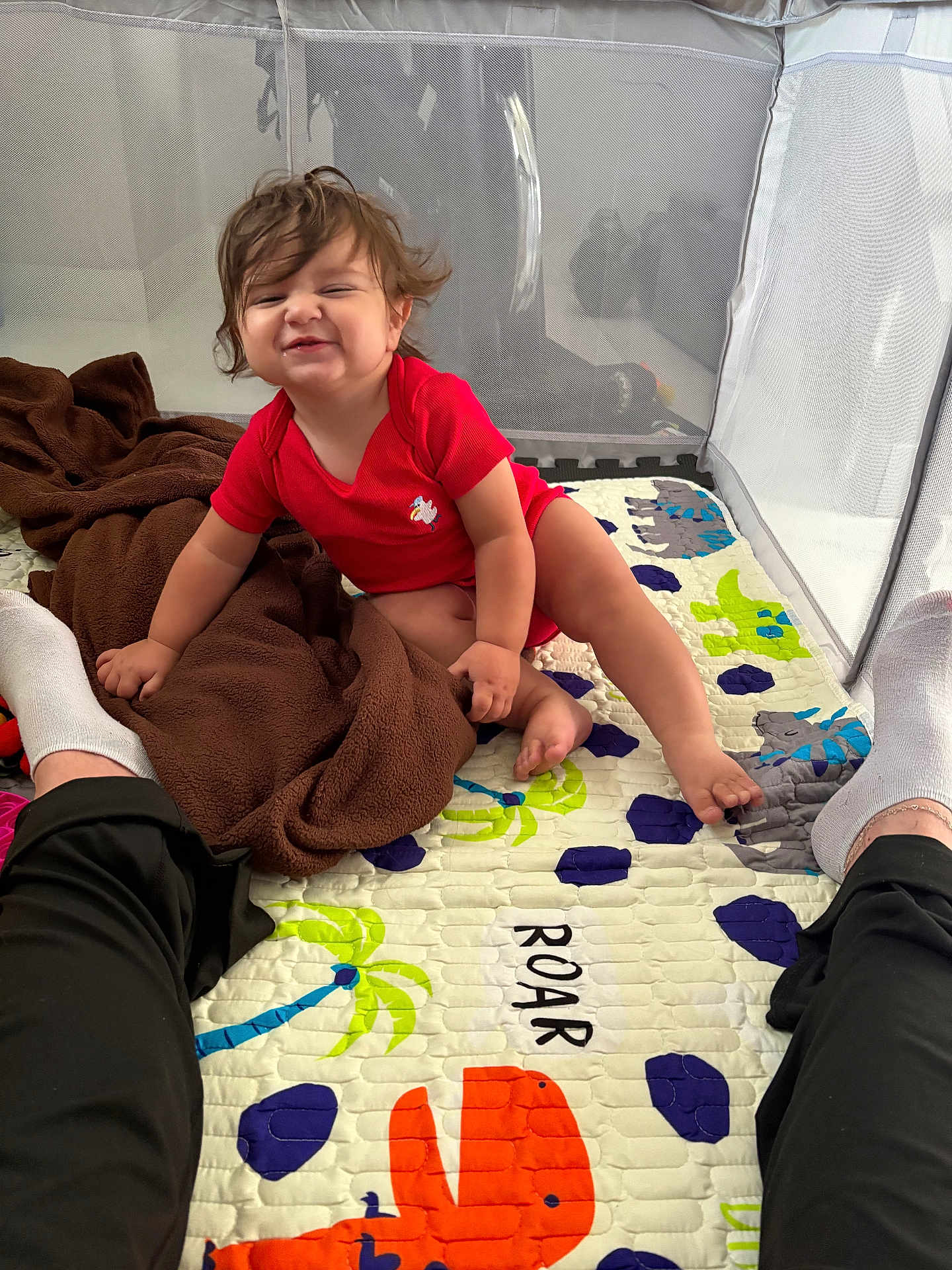 Adonis joined the competition — help win amazing prizes! toddler, child, red_onesie, playpen, colorful_mat, dinosaur_pattern, blanket, brown_blanket, happy, smiling, sitting, indoor, person, legs, socks, hair, cute, baby, fun, playtime