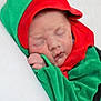 baby, sleeping, infant, child, green_clothing, red_clothing, hood, soft_texture, cute, peaceful, portrait, closeup, face, hand, resting, newborn, indoors, cozy, blanket, wrapped
