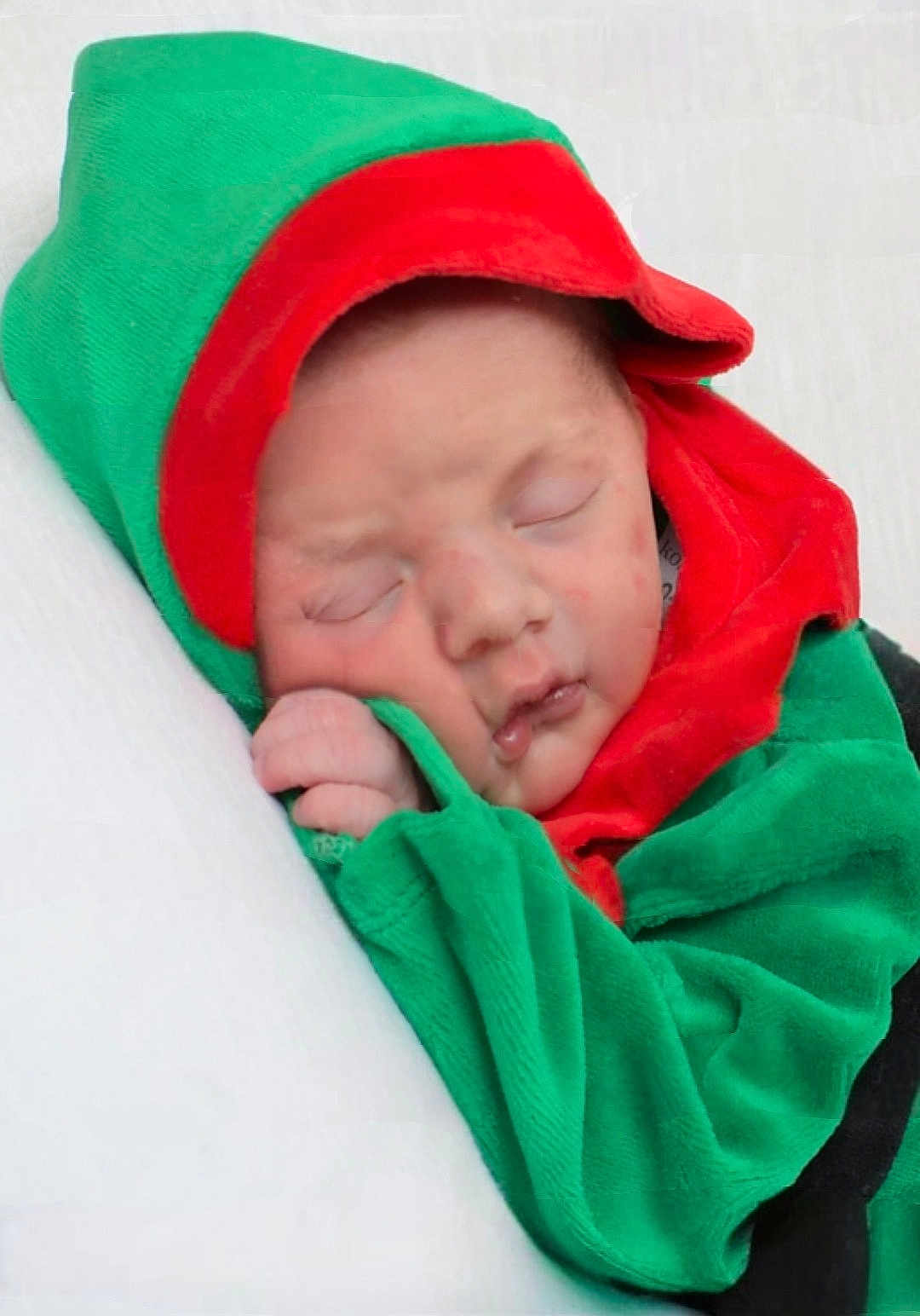 Dallas is registered to the contest to win money with this photo: baby, sleeping, infant, child, green_clothing, red_clothing, hood, soft_texture, cute, peaceful, portrait, closeup, face, hand, resting, newborn, indoors, cozy, blanket, wrapped
