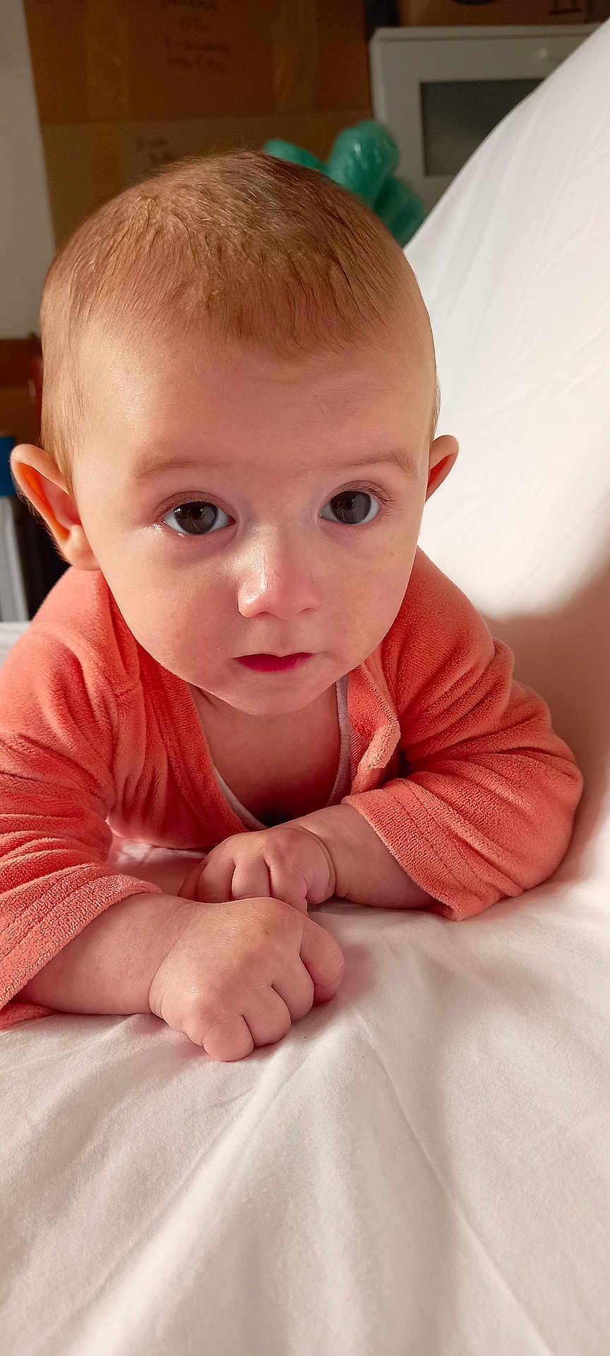 Mathys participe au concours pour gagner de l'argent avec cette photo : baby, infant, child, face, expression, eyes, hands, orange_clothing, bed, white_bedspread, indoors, portrait, cute, young, skin, person, head, lying_down, closeup, curious