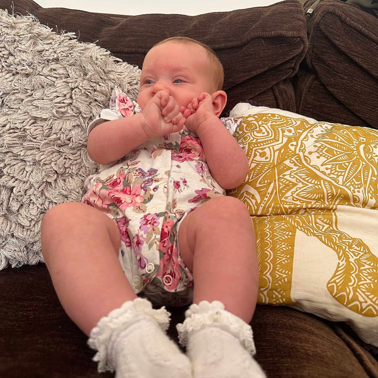 Elarah is registered to the contest to win money with this photo: baby, brown, child, comfort, couch, cozy, cute, face, floral_pattern, furniture, hands, indoor, infant, onesie, person, pillow, relaxing, socks, soft_texture, white