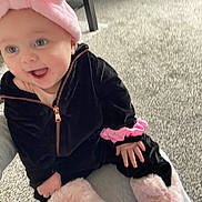 Kyla is registered to the contest to win money with this photo: baby, child, infant, pink_headband, black_outfit, fluffy_boots, happy, smiling, carpet, indoor, person, hand, seated, cute, cozy, playful, young_child, apparel, headwear, footwear