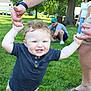 Greyson joined the competition — help win amazing prizes! toddler, child, curly_hair, blue_eyes, smiling, holding_hands, grass, park, adult, family, outdoor, greenery, casual_clothing, shorts, tshirt, people, sunny, daytime, tree, footwear