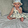 Mckenna is registered to the contest to win money with this photo: baby, child, dress, hat, sitting, bed, pillow, blanket, face, foot, hand, curious, indoors, cute, infant, smiling, person, clothing, soft, home
