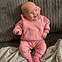 baby, child, pink_hoodie, pink_pants, pink_socks, smiling, happy, couch, blanket, indoors, cozy, seated, infant, face, clothing, person, cute, soft_texture, home, relaxed