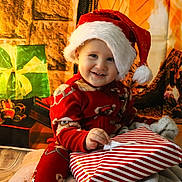 Enzo participe au concours pour gagner de l'argent avec cette photo : toddler, child, santa_hat, red_pajamas, christmas_present, gift_wrapping, holiday_decor, fireplace, christmas_lights, smiling, indoors, festive, cozy, warm_lighting, holiday_season, wrapped_gifts, floor, blanket, happy, portrait