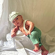 Aaron joined the competition — help win amazing prizes! baby, infant, child, knitted_clothing, cap, green_pants, white_background, fabric, soft_texture, cute, portrait, lying_down, drool, skin, small_hands, small_feet, expression, indoors, person, photography