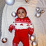 baby, child, infant, red_clothing, knitwear, hat, holiday, christmas, ornaments, silver_baubles, blanket, carpet, festive, cute, lying_down, indoor, portrait, expression, winter_wear, smiling