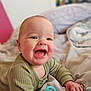 baby, smiling, infant, pacifier, green_clothing, bed, blanket, happy, cute, child, indoors, portrait, face, hand, soft_lighting, closeup, skin, expression, lying_down, cozy