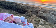 Elina a rejoint le concours — aidez-le/la à gagner de superbes lots ! baby, infant, child, sunset, beach, ocean, rocks, blanket, hat, pacifier, hand, portrait, outdoors, horizon, waves, shore, sky, sun, cozy, serene