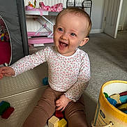 Zara joined the competition — help win amazing prizes! baby, barefoot, bucket, carpet, child, clothing, door, face, floor, happy, home, indoor, leggings, long_sleeve_shirt, play_mat, radiator, sitting, smiling, toys, wooden_blocks