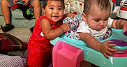 Kamila joined the competition — help win amazing prizes! children, toddlers, baby, smiling, sitting, standing, high_chair, playroom, home, family, siblings, game_controller, couch, blanket, toy, ball, colorful_clothing, red_dress, indoor, portrait