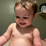 Sophia is registered to the contest to win money with this photo: baby, child, smiling, indoor, skin, hair, cheeks, arms, torso, laundry_basket, shelf, wall, curly_hair, cute, happy, infant, person, portrait, naked_torso, young