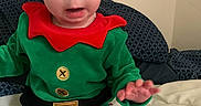 Elizabeth joined the competition — help win amazing prizes! baby, bed, blanket, child, cute, elf_costume, expression, face, festive, green_clothing, hands, holiday_outfit, indoor, person, pillow, portrait, red_collar, sitting, striped_pants, young_child