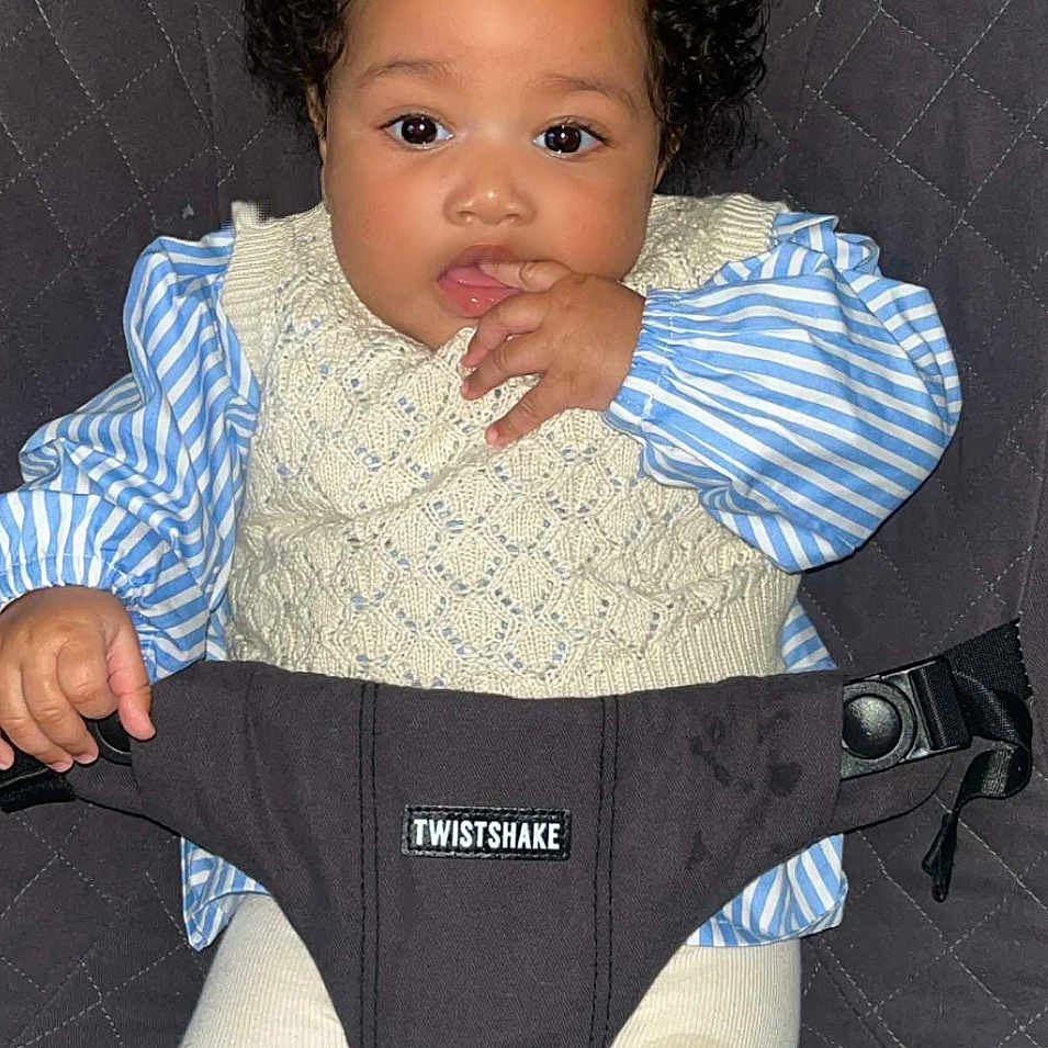 Amaya a rejoint le concours — aidez-le/la à gagner de superbes lots ! adorable, baby, baby_seat, blue_bow, child, clothing, comfort, curly_hair, cute, eyes, face, hand_in_mouth, indoor, infant, knitted_vest, person, portrait, sitting, striped_shirt, white_pants