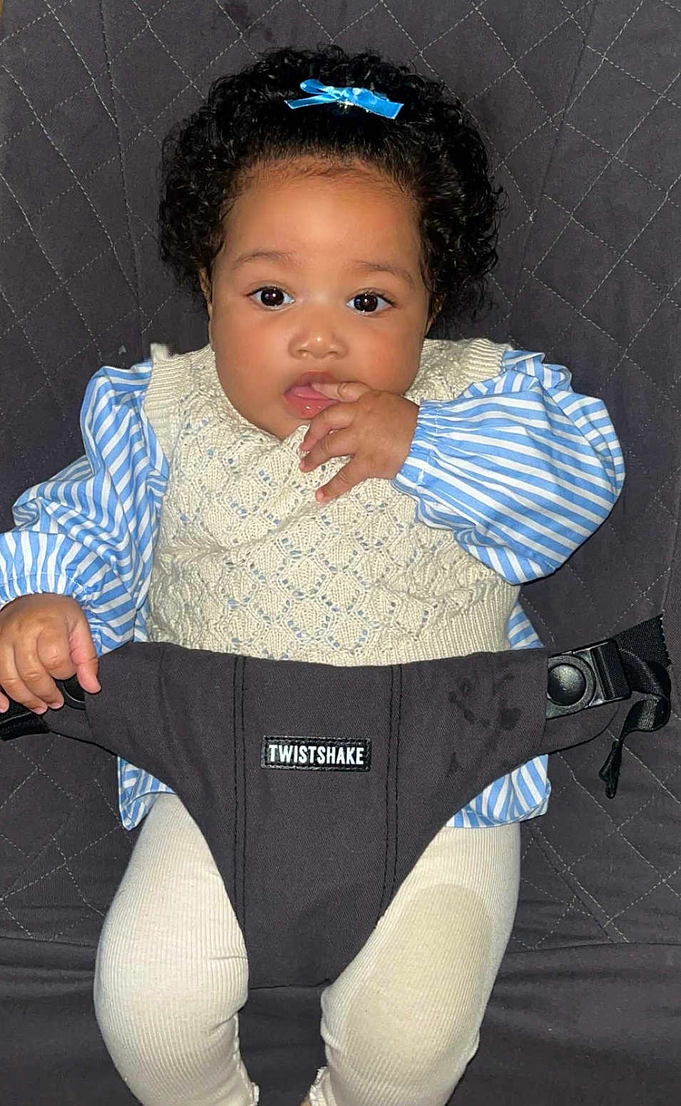 Amaya a rejoint le concours — aidez-le/la à gagner de superbes lots ! baby, child, curly_hair, blue_bow, knitted_vest, striped_shirt, white_pants, baby_seat, comfort, indoor, portrait, cute, sitting, hand_in_mouth, face, eyes, infant, clothing, person, adorable