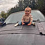 baby, child, car, bmw, hood, outdoor, trees, cloudy_sky, smiling, jeans, socks, topknot, person, vehicle, matte_black, nature, daylight, cute, casual_clothing, portrait