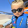 Suzy a rejoint le concours — aidez-le/la à gagner de superbes lots ! toddler, child, sunglasses, life_jacket, boat, outdoor, sunny, water, sea, blue_sky, casual_clothing, cartoon_pattern, yellow_buckle, portrait, young_child, summer, vacation, cute, fashion, leisure