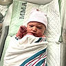 newborn, baby, infant, hospital, bassinet, swaddled, blanket, hat, portrait, face, eyes, fist, lying_down, nursery, medical, crib, textile, striped, indoors, photography