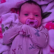 Vivian is registered to the contest to win money with this photo: baby, infant, child, pacifier, portrait, face, eyes, lying_down, blanket, pink, purple, baby_clothing, onesie, patterned_clothing, bows, bed, cozy, indoors, close_up, photograph