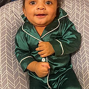 Kashton is registered to the contest to win money with this photo: baby, child, pajamas, green_clothing, smile, face, cushion, indoor, blanket, toy, happy, infant, sitting, cozy, cute, young_child, portrait, person, home, comfort