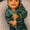 baby, child, pajamas, green_clothing, smile, face, cushion, indoor, blanket, toy, happy, infant, sitting, cozy, cute, young_child, portrait, person, home, comfort