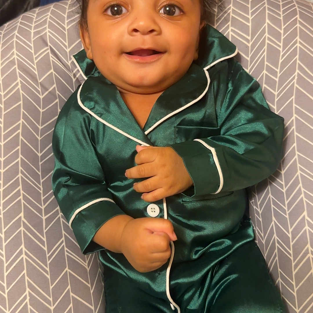Kashton is registered to the contest to win money with this photo: baby, child, pajamas, green_clothing, smile, face, cushion, indoor, blanket, toy, happy, infant, sitting, cozy, cute, young_child, portrait, person, home, comfort