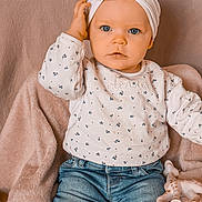 Ava a rejoint le concours — aidez-le/la à gagner de superbes lots ! baby, child, infant, blue_eyes, headband, bow, white_shirt, patterned_clothing, jeans, giraffe_toy, soft_blanket, pink_blanket, seated, cute, portrait, indoor, person, toddler, hand_touching_head, looking_at_camera